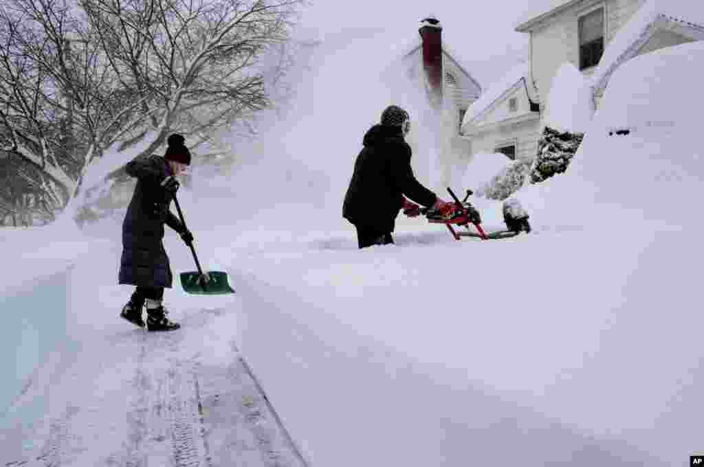 Susan Iannuzzi, left, and Linda Marzell clear a sidewalk after heavy snowfall, on street in Binghamton, New York.
