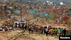 FILE - Residents stand in the foreground of buildings and houses that were destroyed when a vehicle carrying mining explosives detonated along a road in Apiate, Ghana, Jan. 21, 2022. 