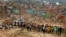 FILE - Residents stand in the foreground of buildings and houses that were destroyed when a vehicle carrying mining explosives detonated along a road in Apiate, Ghana, Jan. 21, 2022. 