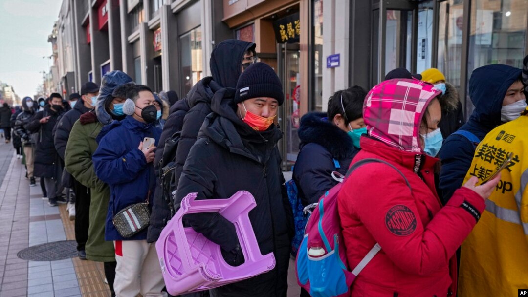 Seorang pria tampak membawa kursi plastik saat mengantre untuk membeli suvenir Olimpiade Musim Dingin Beijing di salah satu toko di Beijing, pada 7 Februari 2022. (Foto: AP/Andy Wong)