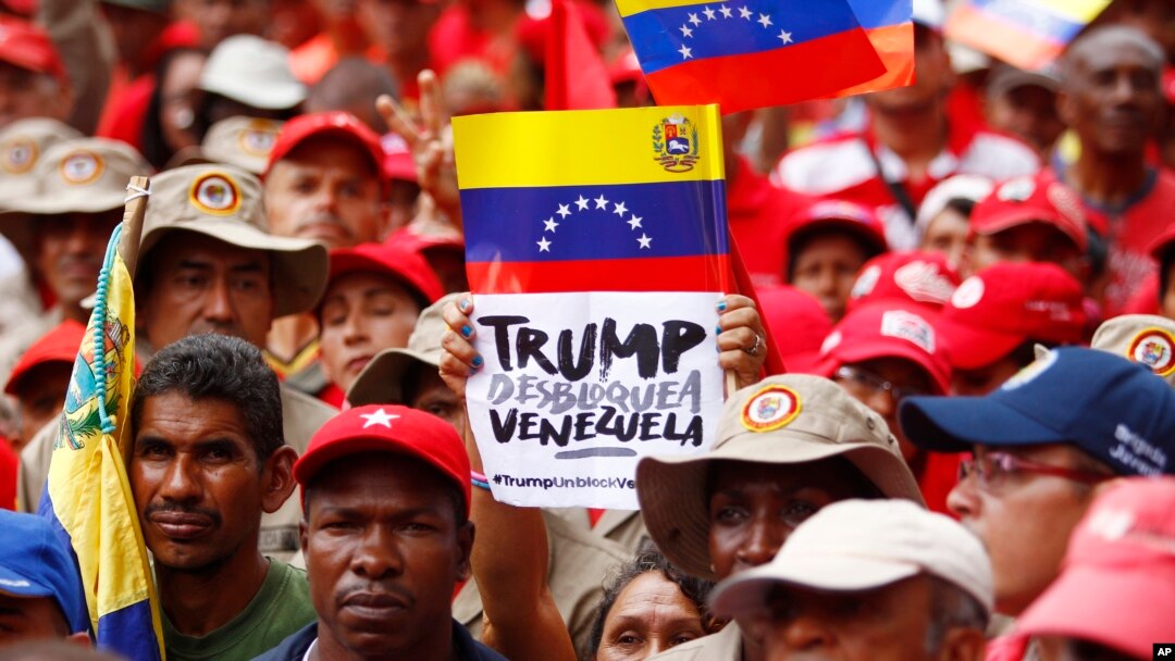 FILE - A demonstrator holds a sign with a message that reads in Spanish: "Trump unblock Venezuela" as members of the Bolivarian militia attend a protest against U.S. sanctions on Venezuela, in Caracas, Venezuela, Aug. 7, 2019. 