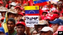 A demonstrator holds a sign with a message that reads in Spanish: "Trump unblock Venezuela" as members of the Bolivarian militia attend a protest against U.S. sanctions on Venezuela, in Caracas, Venezuela, Aug. 7, 2019. 