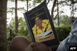 FILE - A man reads a copy of "The Greedy Barbarian," a book authored by Ugandan novelist Kakwenza Rukirabashaija, in Kampala, Jan. 25, 2022.
