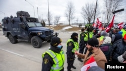 FILE - Protesters interact with police officers who stand guard on a street after Windsor Police said that they are starting to enforce a court order to clear truckers and supporters blocking access to the Ambassador Bridge, Feb. 13, 2022.