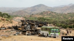 FILE - Villagers return from a market to Yechila town in south central Tigray walking past scores of burned vehicles, in Tigray, Ethiopia, July 10, 2021. 