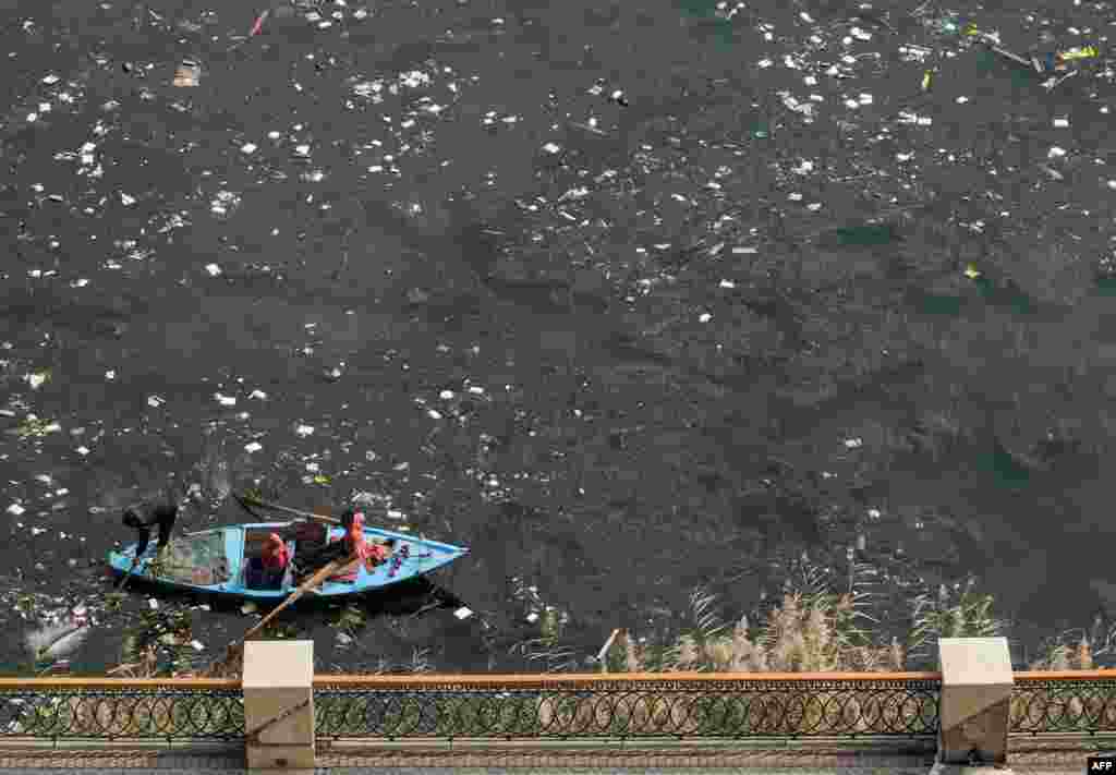 A man rows a fishing boat in the plastic-filled Nile river water off the shore in the Egyptian capital&#39;s twin city of Giza.