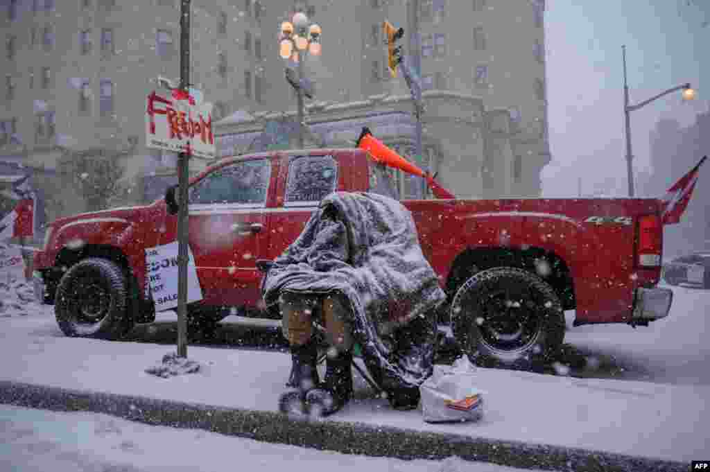 Um manifestante cobre-se com uma manta no meio de uma queda de neve durante um protesto dos camionistas contra regras sanitárias da pandemias e contra o governo de Trudeau, fora do parlamento do Canadá em Otawa, Ontário, 12 de Fevereiro de 2022.