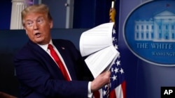 FILE - Then-President Donald Trump holds up papers as he speaks in the James Brady Press Briefing Room of the White House on April 20, 2020, in Washington.