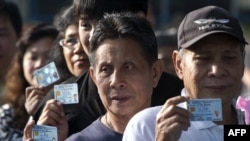 FILE- Thai voters show their ID cards as they queue to cast their ballot at a polling station in Bangkok on February 2, 2014.