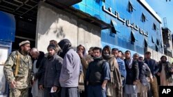 Seorang tentara Taliban berjaga di depan orang-orang yang menunggu untuk masuk ke bank, di Kabul, Afghanistan, 13 Februari 2022. (Foto: AP)