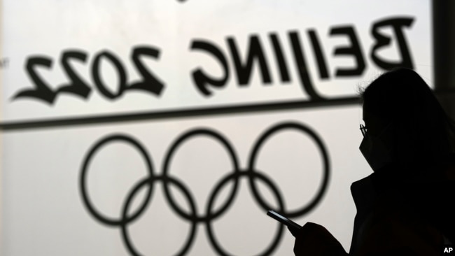 A woman looks at her phone as she passes an Olympic logo inside the main media center for the Beijing Winter Olympics Tuesday, Jan. 18, 2022, in Beijing. (AP Photo/David J. Phillip)