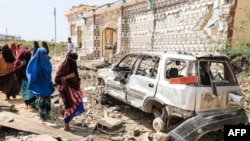 Women walk past a destroyed house and the wreckage of a car following an attack by Al-Shabaab militant to a police station on the outskirts of Mogadishu, Somalia, Feb. 16, 2022. 
