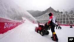 Workers clear snow from inside the finish area of the alpine ski venue speed course at the 2022 Winter Olympics, Feb. 13, 2022, in the Yanqing district of Beijing. 