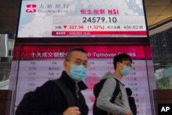 Orang-orang berjalan melewati papan elektronik bank yang menunjukkan indeks saham Hong Kong di Bursa Efek Hong Kong Senin, 14 Februari 2022. (Foto: AP)