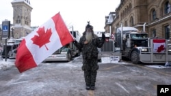 Yon manifestan kanpe devan yon gwoup kamyon nan Otawa, Kanada, 3 Fevriye 2022. 