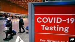 FILE - Travelers pass a sign near a COVID-19 testing site in Terminal E at Logan Airport, in Boston, Dec. 21, 2021. 