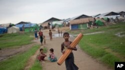 FILE - A Rohingya boy walks with a mat as children play in the background at Dar Paing camp for Muslim refugees in north of Sittwe, western Rakhine State, Myanmar. 