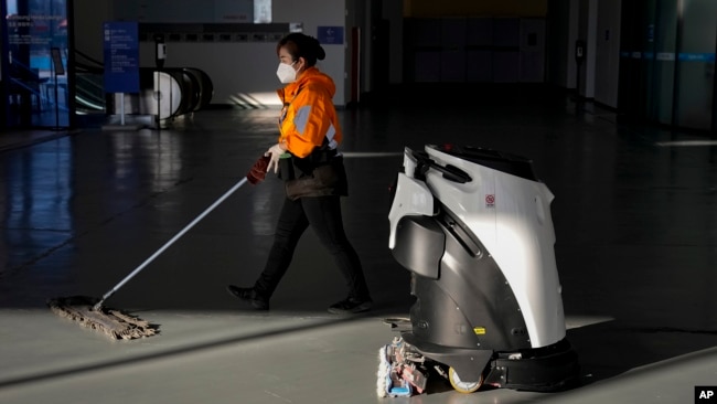A worker and a robot clean the floor of the main media center ahead of the 2022 Winter Olympics, Tuesday, Feb. 1, 2022, in Beijing. (AP Photo/Jae C. Hong)