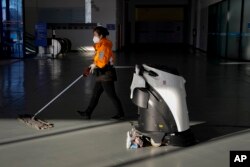 A worker and a robot clean the floor of the main media center ahead of the 2022 Winter Olympics, Tuesday, Feb. 1, 2022, in Beijing. (AP Photo/Jae C. Hong)