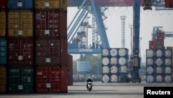 Seorang pekerja mengendarai sepeda motor melewati tumpukan peti kemas di Terminal Peti Kemas IPC Pelabuhan Tanjung Priok, Jakarta, 4 November 2021. (Foto: REUTERS/Willy Kurniawan)