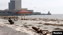 A man sits on a bench overlooking a beach covered in debris scattered by Hurricane Nate, in Biloxi, Mississippi, Oct. 8, 2017.