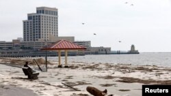 A man sits on a bench overlooking a beach covered in debris scattered by Hurricane Nate, in Biloxi, Mississippi, Oct. 8, 2017.