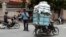 A Cambodian man, right, drive his motorbike overloaded with vegetable sacks as he passes a traffic police officer, center, in Phnom Penh, Cambodia, Tuesday, Aug. 25, 2015. (AP Photo/Heng Sinith)