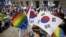 An activist holds up a rainbow-colored fan and a South Korean national flag as gay pride festival participants face Christians opposed to homosexuality in central Seoul, South Korea, June 28, 2015.