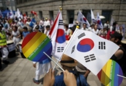 An activist holds up a rainbow-colored fan and a South Korean national flag as gay pride festival participants face Christians opposed to homosexuality in central Seoul, South Korea, June 28, 2015.