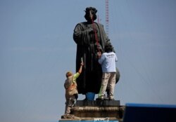 FILE - Workers clean the statue of Italian explorer Christopher Columbus, surrounded by metal fencing during Columbus Day, in Mexico City, Mexico, October 12, 2020.