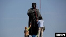 FILE - Workers clean the statue of Italian explorer Christopher Columbus, surrounded by metal fencing during Columbus Day, in Mexico City, Mexico, October 12, 2020.