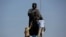 FILE - Workers clean the statue of Italian explorer Christopher Columbus, surrounded by metal fencing during Columbus Day, in Mexico City, Mexico, October 12, 2020.