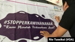 Seorang laki-laki membubuhkan pesan menolak perkawinan anak di atas spanduk yang dipajang dalam Festival Kabupaten/Kota Layak Anak (KLA) yang digelar di Bandung, Minggu (16/12/2018) siang. (Foto: Rio Tuasikal/VOA)