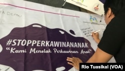 Seorang laki-laki membubuhkan pesan menolak perkawinan anak di atas spanduk yang dipajang dalam Festival Kabupaten/Kota Layak Anak (KLA) yang digelar di Bandung, Minggu (16/12/2018) siang. (Foto: Rio Tuasikal/VOA)