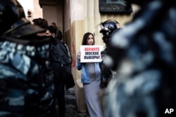 FILE - A woman holds a poster reading "Give Moscow Back Its Elections!" in front of police during a protest in Moscow, Russia, Aug. 10, 2019.