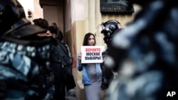 FILE - In this file photo taken on Saturday, Aug. 10, 2019, A woman holds a poster reading "Give us back our elections in Moscow!" in front of police during a protest in Moscow, Russia. Ella Pamfilova, head of Russian Central Election Commission,…