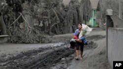 Seorang perempuan membawa patung bayi Yesus sementara dia melewati daerah yang diselimuti abu vulkanik dari letusan Gunung Taal di Boso-Boso, provinsi Batangas, Filipina (14/1). 