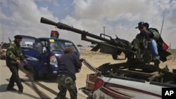 A Libyan rebel, dressed as a cowboy, mans an anti-aircraft gun as fellow rebels load ammunition as they wait for the signal to advance at an intersection just outside Brega, Libya, Sunday, April 3, 2011. Libyan rebels want to install a parliamentary demo