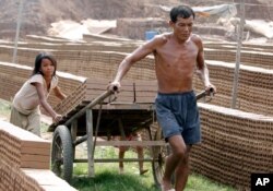 FILE - A Cambodian man and his daughter move a cart loaded with bricks at a brick factory in Chheuteal village, Kandal province, north of Phnom Penh, Cambodia, May 2, 2011.