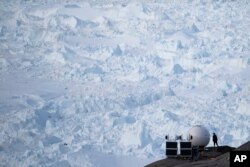 In this Aug. 16, 2019, photo, a woman stands next to an antenna at an NYU base camp at the Helheim glacier in Greenland.