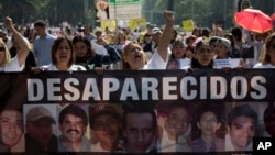 FILE - Women carry a banner calling attention to the cases of people who have gone missing in the fight against drug cartels and organized crime, demanding authorities locate their loved ones, May 10, 2018.