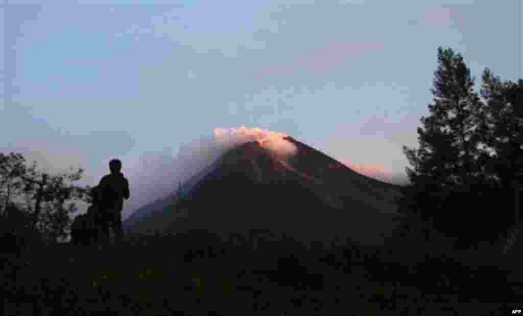 A villager watches Mount Merapi in Kaliadem, Yogyakarta, Indonesia, Tuesday, Oct. 26, 2010. Indonesia's most volatile volcano started erupting Tuesday, after scientists warned that pressure building beneath its dome could trigger the most powerful eruptio