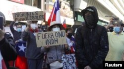 Manifestantes sostienen pancartas que dicen "No más ONU" y "Fuera migrantes ilegales", junto a un manifestante encapuchado a favor de los migrantes durante una protesta contra la inmigración en Santiago de Chile, el 2 de octubre de 2021.