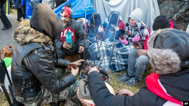 People demonstrating against COVID-19 restrictions stay warm with blankets and a fire during frigid temperatures on Wellington Street in the Parliament Hill area of Ottawa, Ontario, Canada, on Sunday, Feb. 13, 2022. (AP Photo/Ted Shaffrey)