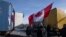Demonstrators, one holding a Canadian flag, stand next some of the 20 trucks which blocked one entrance to the government buildings, rear, in The Hague, Netherlands, Saturday, Feb. 12, 2022, to protest against COVID-19 restrictions.