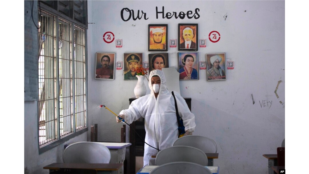 Seorang pekerja menyemprotkan disinfektan di dalam ruang kelas yang kosong setelah ditemukan kasus COVID-19 di sebuah sekolah di Medan, Sumatera Utara, Jumat, 11 Februari 2022. (Foto: AP)