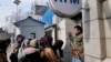 An Afghan security guard holds his AK-47 rifle, as women lineup outside an ATM machine to withdraw money, in Kabul, Afghanistan, Feb. 8, 2022.