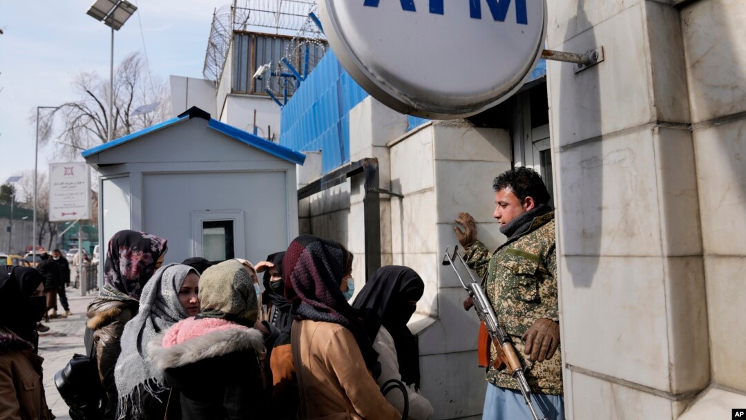 An Afghan security guard holds his AK-47 rifle, as women lineup outside an ATM machine to withdraw money, in Kabul, Afghanistan, Feb. 8, 2022.