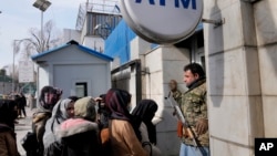 An Afghan security guard holds his AK-47 rifle, as women lineup outside an ATM machine to withdraw money, in Kabul, Afghanistan, Feb. 8, 2022.