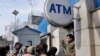 An Afghan security guard holds his AK-47 rifle, as women lineup outside an ATM machine to withdraw money, in Kabul, Afghanistan, Feb. 8, 2022.